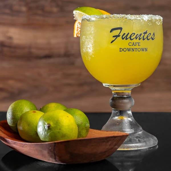 A Fuentes Cafe Downtown margarita with a salted rim, lime, and orange slice, next to a bowl of limes.