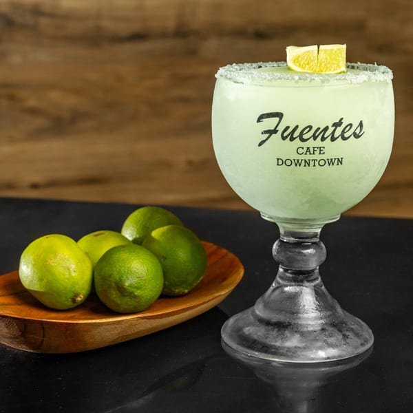 A Fuentes Cafe Downtown margarita with a salted rim and lime, next to a wooden bowl of limes.