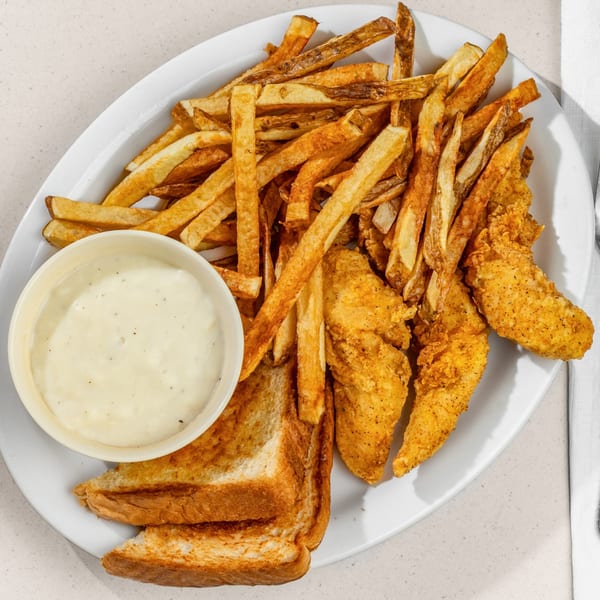 Fried chicken tenders, golden fries, Texas toast, and a side of creamy gravy on a white plate.