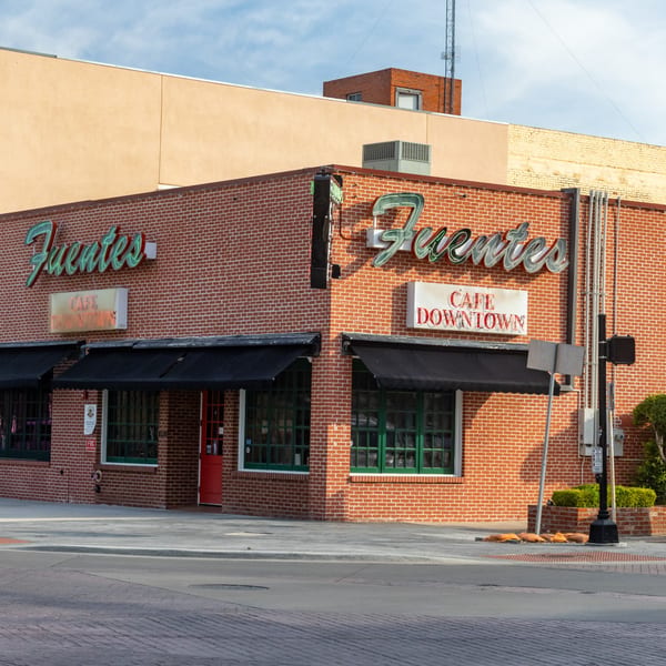 Exterior of Fuentes Cafe Downtown, a brick building with black awnings and green neon signs.