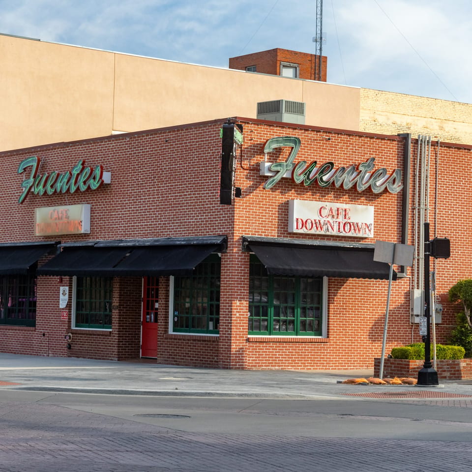 Exterior of Fuentes Cafe Downtown, a brick building with black awnings and green neon signs.