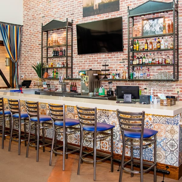 A long bar with blue-seated stools, a brick wall, and shelves of liquor bottles at Fuentes Cafe Downtown.